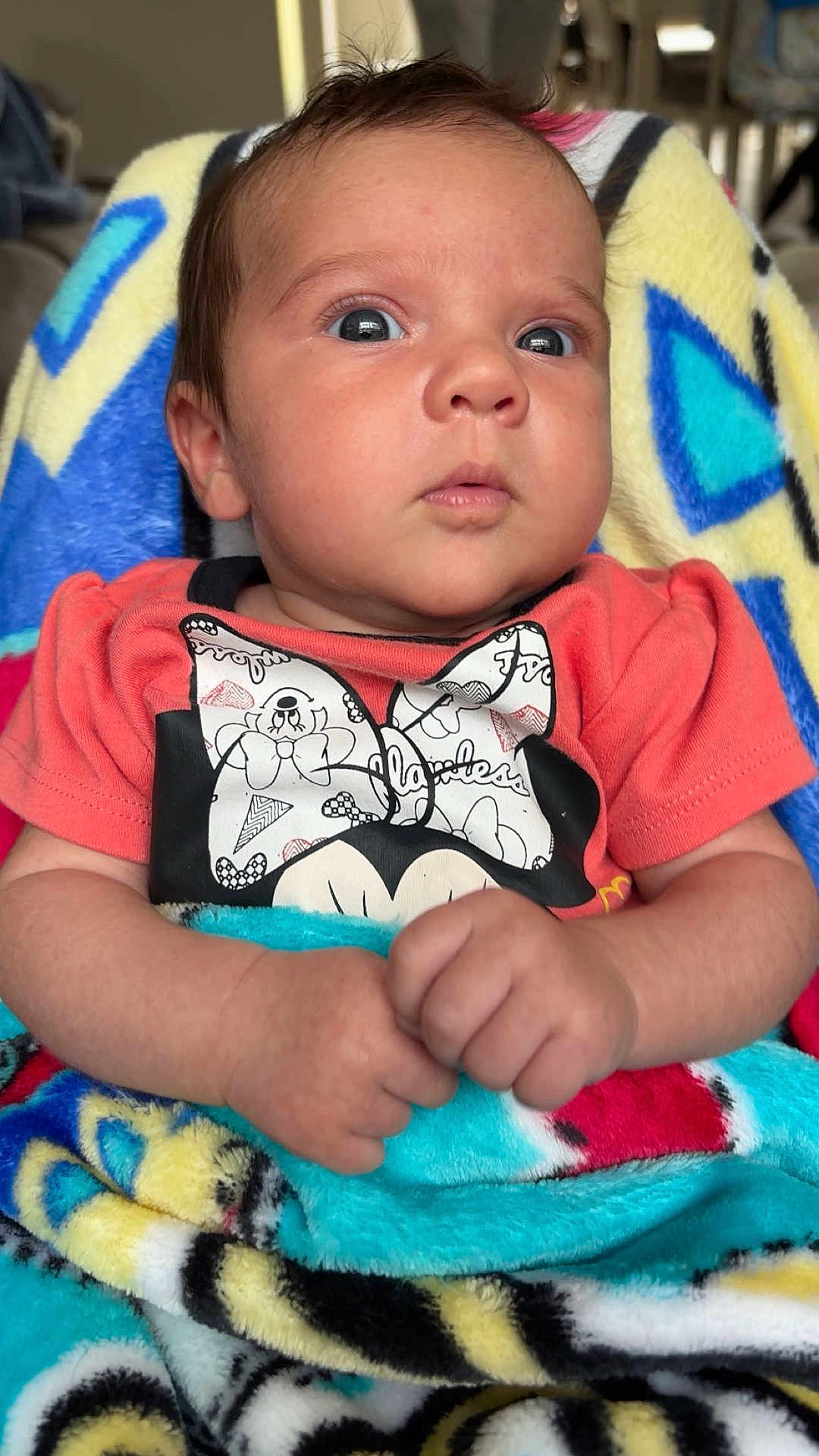 Oak is registered to the contest to win money with this photo: baby, infant, blanket, colorful, clothing, orange_shirt, bow, face, hands, cute, wide_eyes, indoor, person, portrait, soft_texture, young_child, cozy, wrapped, seated, expression