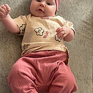 Ariella is registered to the contest to win money with this photo: baby, infant, headband, pink_clothing, pants, tshirt, flower_pattern, lying_down, barefoot, cute, chubby, indoors, soft_texture, skin, face, person, child, young, expression, portrait