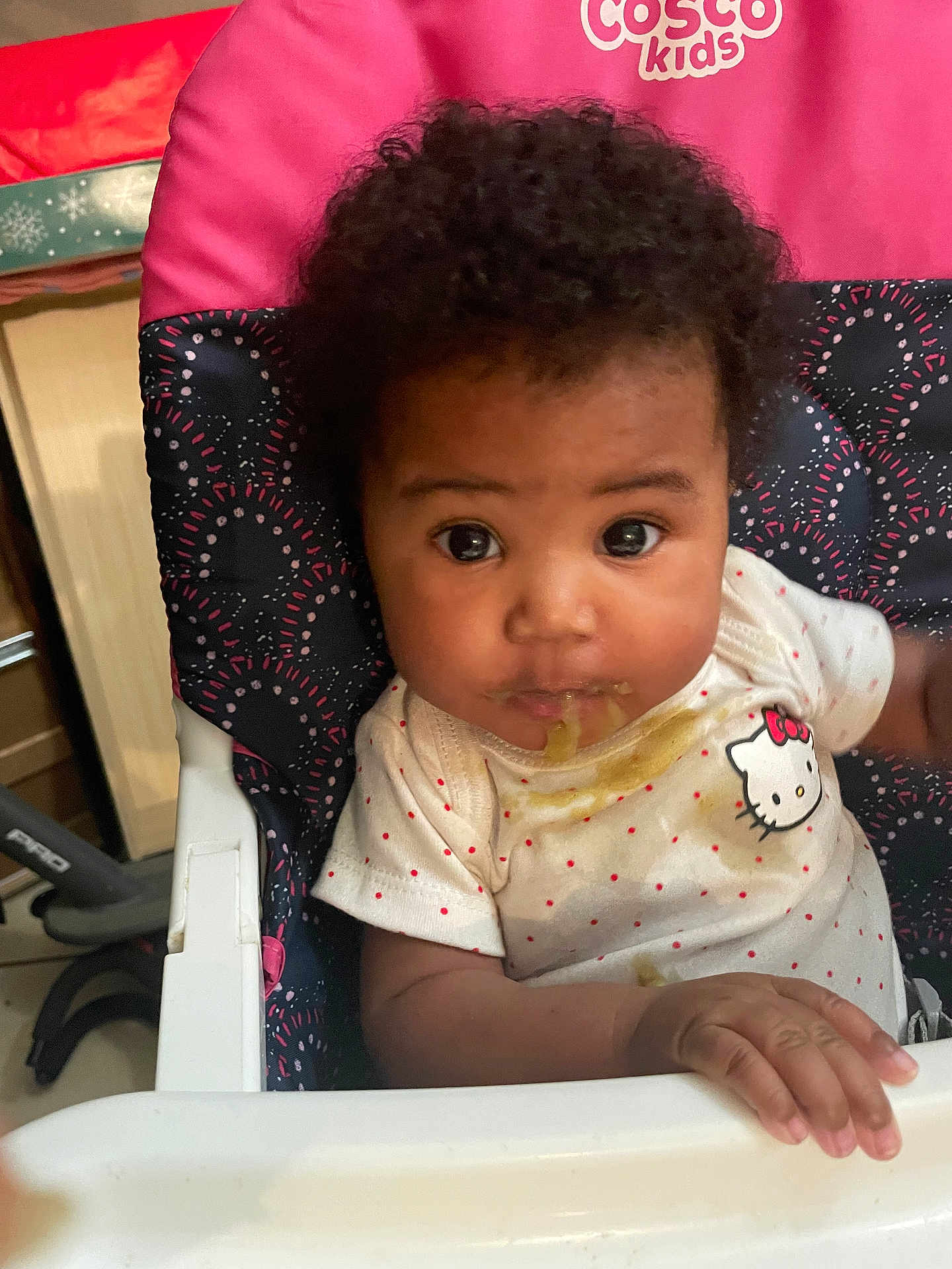 Dannique is registered to the contest to win money with this photo: baby, child, closeup, curly_hair, cute, expression, face, feeding, food, hand, hello_kitty, high_chair, indoor, infant, looking, messy, person, seat, shirt, young