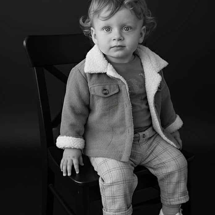 Aylan participe au concours pour gagner de l'argent avec cette photo : black_and_white, chair, child, clothing, curly_hair, cute, expression, eyes, face, fashion, footwear, indoor, jacket, plaid_pants, portrait, shoes, sitting, studio, toddler, young_child