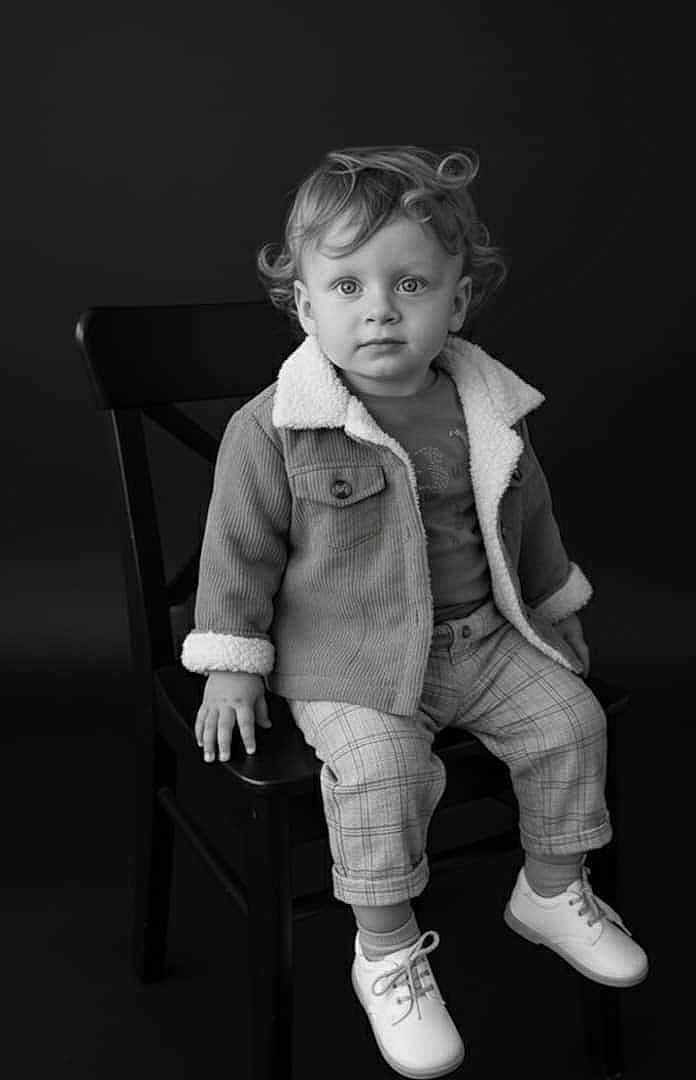 Aylan participe au concours pour gagner de l'argent avec cette photo : toddler, child, curly_hair, jacket, plaid_pants, shoes, chair, portrait, black_and_white, studio, sitting, fashion, cute, young_child, face, eyes, clothing, footwear, indoor, expression