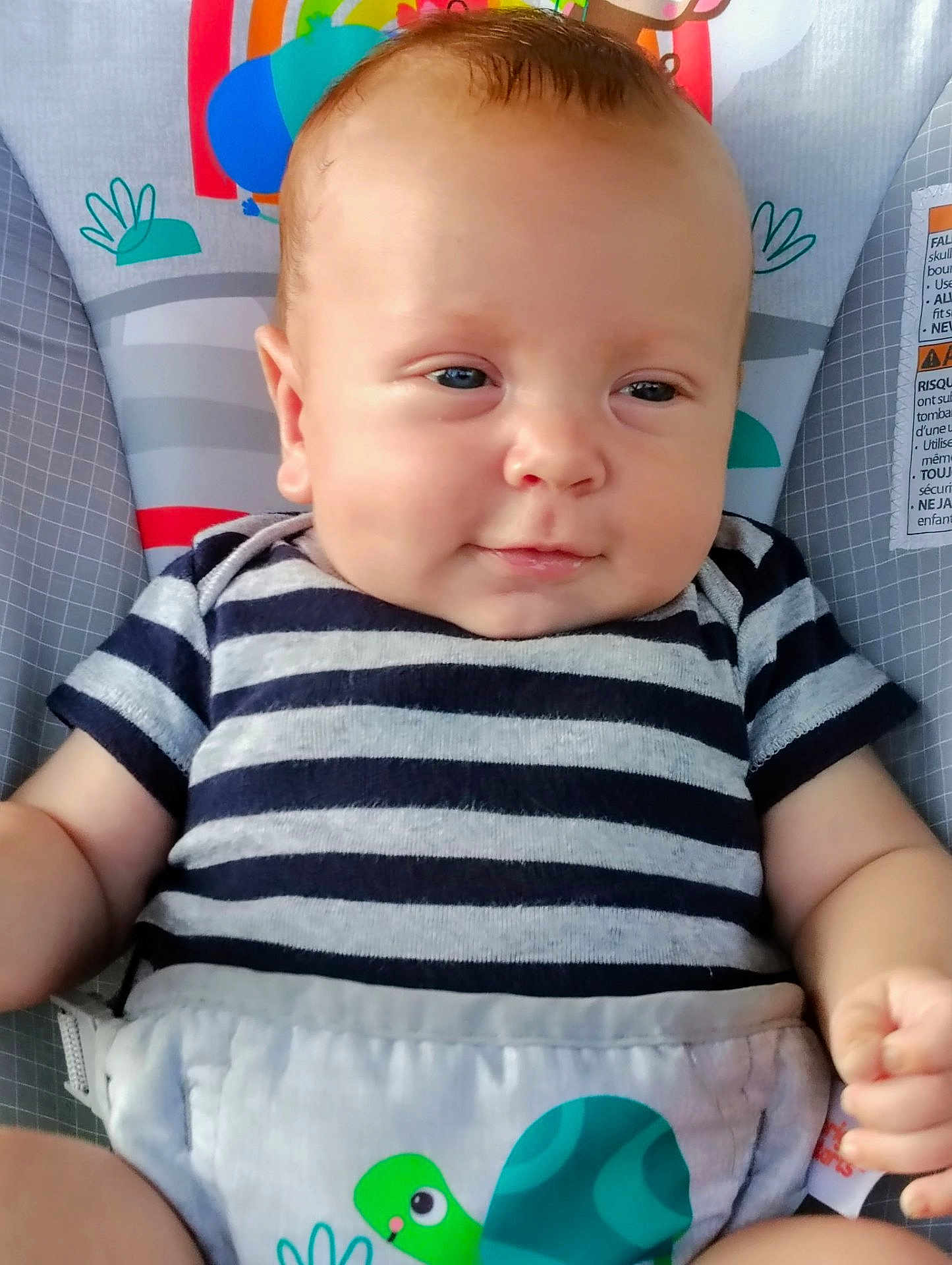 Kayson is registered to the contest to win money with this photo: baby, infant, child, striped_shirt, seat, colorful, smile, face, skin, arm, hand, clothing, cute, indoor, young, portrait, baby_seat, comfort, pattern, sitting