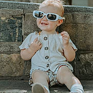 Kira is registered to the contest to win money with this photo: child, toddler, sunglasses, smile, bench, stone_wall, outdoor, summer, shorts, shirt, shoes, socks, portrait, happy, cute, person, sitting, sunlight, accessory, background_blur
