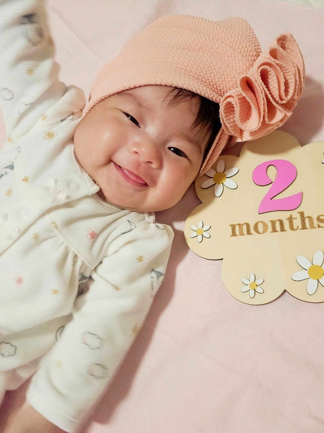 Kassandra is registered to the contest to win money with this photo: baby, infant, smiling, headband, pink, flower_sign, months, cute, lying_down, white_clothing, soft_texture, happy, portrait, closeup, child, adorable, indoor, celebration, two_months, newborn