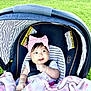 baby, car_seat, pink_bow, blanket, smiling, child, outdoor, grass, infant, headband, seatbelt, striped, happy, person, cute, child_seat, toddler, sunny, nature, portrait