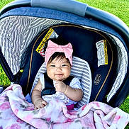 Kassandra is registered to the contest to win money with this photo: baby, car_seat, blanket, pink_bow, headband, smiling, outdoor, grass, child, infant, happy, seatbelt, striped_pattern, clothing, cute, portrait, young_child, sunlight, baby_girl, soft_texture