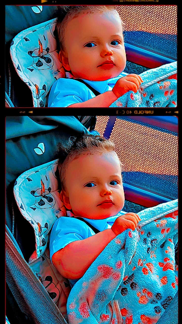 Sören a rejoint le concours — aidez-le/la à gagner de superbes lots ! baby, child, blanket, stroller, blue_shirt, face, infant, hand, seated, patterned_blanket, curly_hair, indoor, portrait, comfort, cute, young_child, looking_at_camera, colorful, fabric, expression