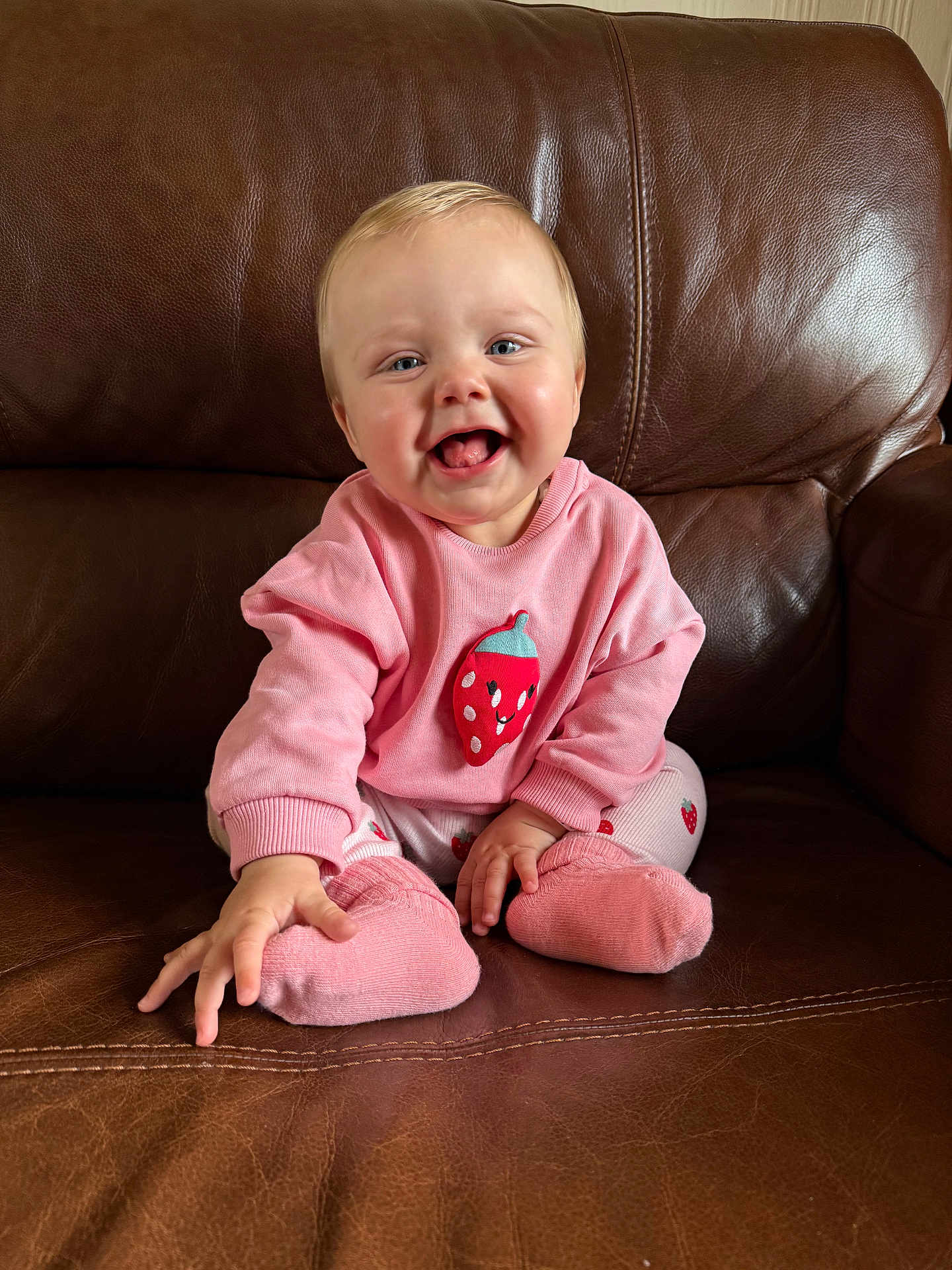 Freya joined the competition — help win amazing prizes! baby, child, pink_clothing, strawberry_design, socks, smiling, happy, sitting, leather_couch, indoor, cute, portrait, young_child, infant, face, hands, feet, cozy, home, casual