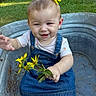 baby, child, toddler, smiling, portrait, outdoor, garden, grass, flowers, yellow_flowers, flower_hair_accessory, denim_overalls, pink_shirt, metal_tub, sitting, bouquet, backyard, greenery, sunlight, happy