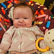 Delilah is registered to the contest to win money with this photo: baby, infant, smile, cute, onesie, polar_bear_pattern, plush_toy, colorful_cushion, indoor, happy, child, face, person, toy, seated, soft_toys, furniture, closeup, portrait, cozy