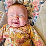 baby, smile, infant, face, clothing, floral_pattern, seat, cushion, happy, child, portrait, indoors, cute, young, person, apparel, fabric, comfort, hair, expression