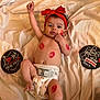 baby, infant, diaper, red_headband, lipstick_marks, blanket, love_sign, moon_sign, smiling, lying_down, cute, face, hand, foot, skin, cheek, playful, happy, indoors, soft_texture