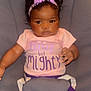 Ilyes is registered to the contest to win money with this photo: baby, child, seat, headband, purple_clothing, pink_shirt, text_on_shirt, indoor, infant, sitting, cute, young_child, clothing, fabric, person, portrait, baby_girl, seat_belt, smiling, hair