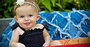 Raylan is registered to the contest to win money with this photo: baby, child, face, headband, flower, blue_eyes, black_clothing, crate, red, coca_cola, outdoor, greenery, blanket, smile, portrait, cute, summer, nature, infant, happy
