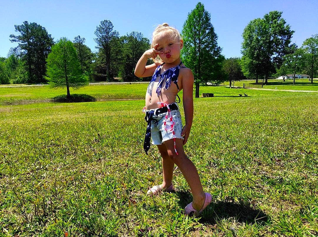 Brailie Kay is registered to the contest to win money with this photo: baby_toddler_clothing, botany, grass, grassland, groundcover, happy, landscape, leaf, leisure, mammal, natural_environment, natural_landscape, nature, people_in_nature, person, plant, sky, smile, sunlight, toddler