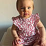 baby, blue_eyes, child, clothing, curious_expression, cushion, face, flower_pattern, foot, hand, indoor, pony_tail, portrait, red_hair_tie, sitting, skin, soft_light, toddler, white_outfit, young