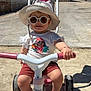 building, child, footwear, fun, handlebars, hat, outdoor, pavement, play, shadow, shorts, smiling, summer, sunglasses, sunny, toddler, toy, tree, tricycle, tshirt