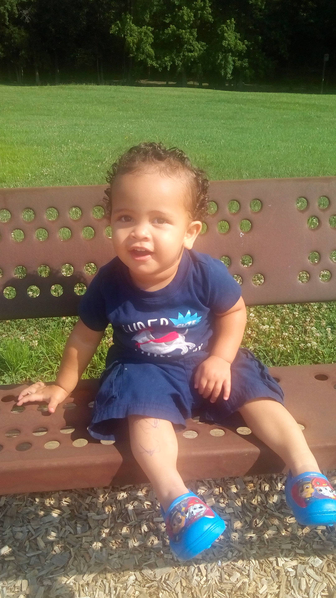 Danilo is registered to the contest to win money with this photo: blue, boy, child, day, facial_expression, fun, grass, infant, leisure, outdoor_play_equipment, person, plant, play, playground, public_space, sitting, smile, standing, summer, toddler