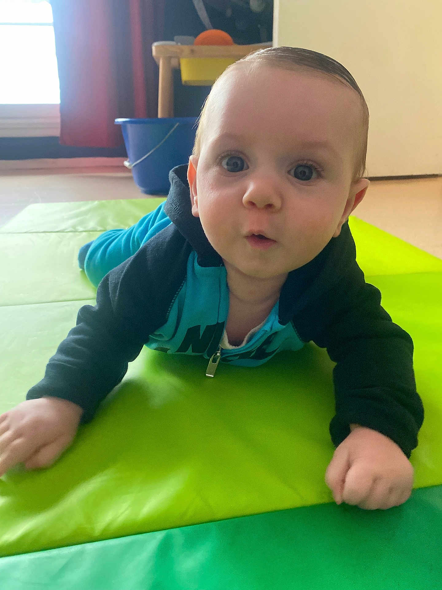Thiago participe au concours pour gagner de l'argent avec cette photo : baby, child, crawling, blue_eyes, hoodie, indoor, mat, curious, expression, floor, toy, bucket, person, young_child, face, hands, clothing, bright_colors, home, casual
