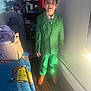 Ezekiel is registered to the contest to win money with this photo: child, boy, green_suit, tie, indoors, smiling, missing_tooth, wooden_floor, blanket, cartoon_character, bag, furniture, shelf, clothing, light, wall, power_outlet, person, happy, portrait