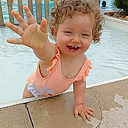 Giulia participe au concours pour gagner de l'argent avec cette photo : toddler, child, pool, water, swimsuit, curly_hair, smiling, happy, outdoor, summer, playful, baby, person, splash, hand, concrete, umbrella, fence, nature, daytime