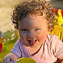 Giulia participe au concours pour gagner de l'argent avec cette photo : toddler, child, curly_hair, blue_eyes, tongue_out, pink_shirt, toy, hand, sunlight, playful, happy, close_up, face, smile, indoors, baby, person, bright_colors, cheeks, cute