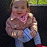 baby, child, smiling, outdoor, seat, jacket, scarf, hands, clothing, face, person, sunlight, election_card, patterned_pants, red_socks, woven_chair, happy, cute, portrait, daylight