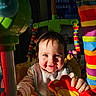 toddler, child, smiling, toy, play_area, colorful, rainbow_stripes, green_plastic, indoors, baby, happy, face, hand, clothing, bib, sunlight, portrait, playtime, infant, cute