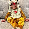 baby, child, puppy_costume, costume, smiling, sitting, couch, indoors, portrait, floppy_ears, tongue, yellow_clothing, onesie, happy, cute, infant, face, toy_costume, living_room, photography
