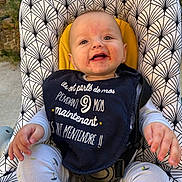 Julio participe au concours pour gagner de l'argent avec cette photo : baby, child, smiling, bib, baby_seat, patterned_fabric, outdoor, happy, face, clothing, infant, seatbelt, person, cute, playful, toddler, nature, sunlight, closeup, hands