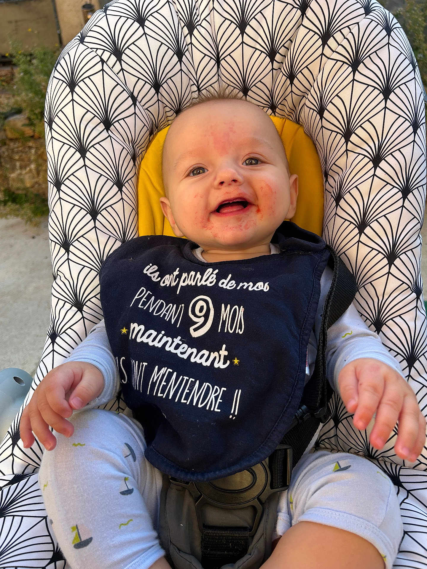 Julio participe au concours pour gagner de l'argent avec cette photo : baby, child, smiling, bib, baby_seat, patterned_fabric, outdoor, happy, face, clothing, infant, seatbelt, person, cute, playful, toddler, nature, sunlight, closeup, hands