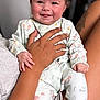 Margot is registered to the contest to win money with this photo: baby, child, smiling, floral_pajamas, tattoo, hand, indoor, person, couch, holding, happy, infant, face, legs, sitting, skin, comfort, portrait, cute, family