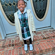 Serenity is registered to the contest to win money with this photo: black_hair, brick_steps, casual_wear, child, coat, cute, door, earrings, fashion, front_door, happy, leggings, outdoor, person, plaid_dress, portrait, smiling, sneakers, standing, young