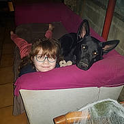 Ares participe au concours pour gagner de l'argent avec cette photo : girl, dog, glasses, couch, magenta_cloth, black_dog, indoor, relaxed, smile, face, pet, furniture, tile_floor, resting, home, comfort, young, portrait, animal, casual