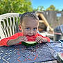 child, boy, watermelon, fruit, eating, outdoor, table, chair, summer, food, happy, blue_eyes, orange_shirt, garden, daylight, fence, plastic_chair, snack, picnic, nature