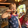 Matthew is registered to the contest to win money with this photo: child, toddler, marshmallow, food, indoor, person, tank_top, pattern, star, stick, face, blue_eyes, hair, hand, table, chair, blurred_background, adult, light, casual_clothing