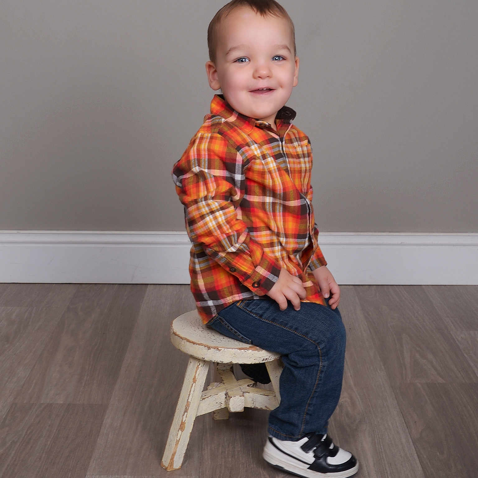 Matthew is registered to the contest to win money with this photo: boy, casual_clothing, child, cute, floor, gray_wall, happy, indoor, jeans, plaid_shirt, portrait, seated, small_person, smiling, sneakers, stool, studio, toddler, wooden_floor, young_child