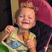Cain is registered to the contest to win money with this photo: baby, chicken_drumstick, child, curly_hair, eating, family_photo, food, green_bowl, happy, high_chair, indoors, laughing, playful, portrait, seated, shark_shirt, smiling, snack, toddler, tray