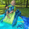 Cain is registered to the contest to win money with this photo: toddler, child, inflatable_pool, swimming, outdoor, grass, trees, dog, blue, yellow, water, summer, play, sunlight, park, fun, slide, curly_hair, person, nature