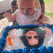 Cain is registered to the contest to win money with this photo: baby, birthday, blue_icing, cake, candle, celebration, child, face, frosting, highchair, icing, messy, nose, outdoor, photo_cake, picnic_table, pizza_box, portrait, smile, toddler