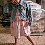 child, denim_jacket, pink_dress, barefoot, carpet, indoor, fan, dresser, toy_pig, playful, pose, blonde_hair, clothing, person, room, floor, head_tilt, furniture, casual, young