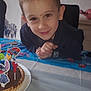 child, boy, smiling, birthday, cake, chocolate_tart, candles, tablecloth, balloons, party, indoor, face, celebration, cartoon_characters, decorations, zebra, happy, young, person, festive