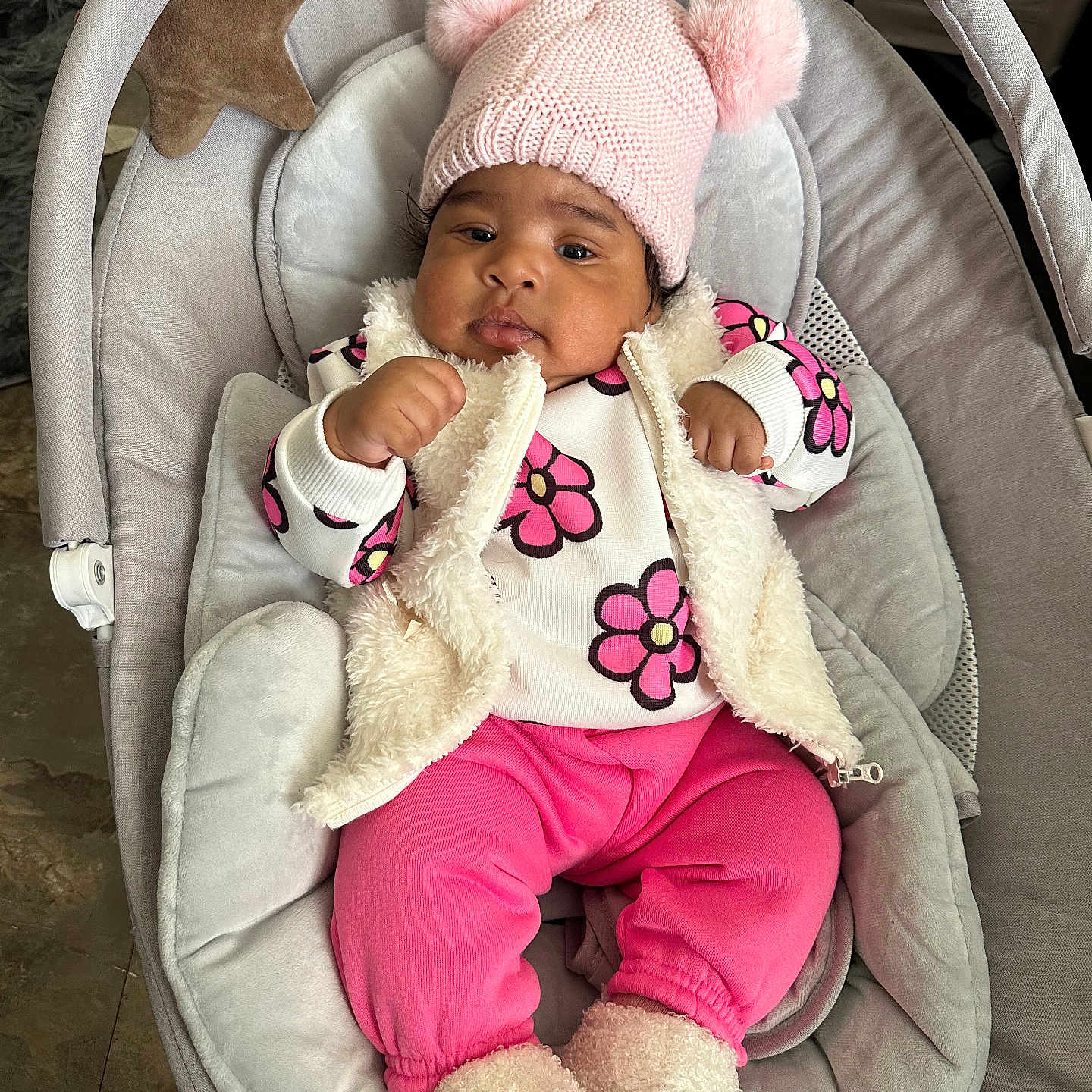 Daniela joined the competition — help win amazing prizes! baby, baby_seat, bear_slippers, child, comfort, cute, face, floor, footwear, fuzzy_vest, hands, hat, indoor, infant, person, pink_clothing, plush_toy, pom_pom, slippers, star_shaped_pillow