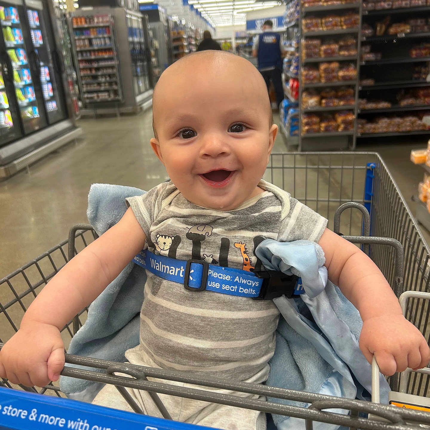 Hudson joined the competition — help win amazing prizes! baby, smiling, shopping_cart, grocery_store, child, striped_clothing, blue_blanket, seatbelt, aisle, shelves, products, floor, person, head, hand, happy, indoor, retail, infant, cute