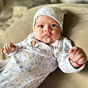 Abby joined the competition — help win amazing prizes! baby, infant, onesie, hat, fist, expression, face, eyes, clothing, couch, blanket, indoor, cute, portrait, child, person, soft_texture, cozy, newborn, comfortable