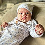 baby, infant, onesie, hat, fist, expression, face, eyes, clothing, couch, blanket, indoor, cute, portrait, child, person, soft_texture, cozy, newborn, comfortable
