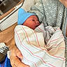 Cameron is registered to the contest to win money with this photo: newborn, baby, parent, hospital, blanket, blue_hat, swaddled, bed, hospital_bed, hand, person, face, smile, indoor, medical, newborn_care, comfort, family, mother, child