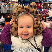 Julliana a rejoint le concours — aidez-le/la à gagner de superbes lots ! accessories, apparel, baby, child, clothing_store, cute, earmuffs, face, fashion, happy, hat, indoor, knitted, leopard_print, purple_sweater, shopping_cart, smiling, toddler, white_vest, winter_clothes