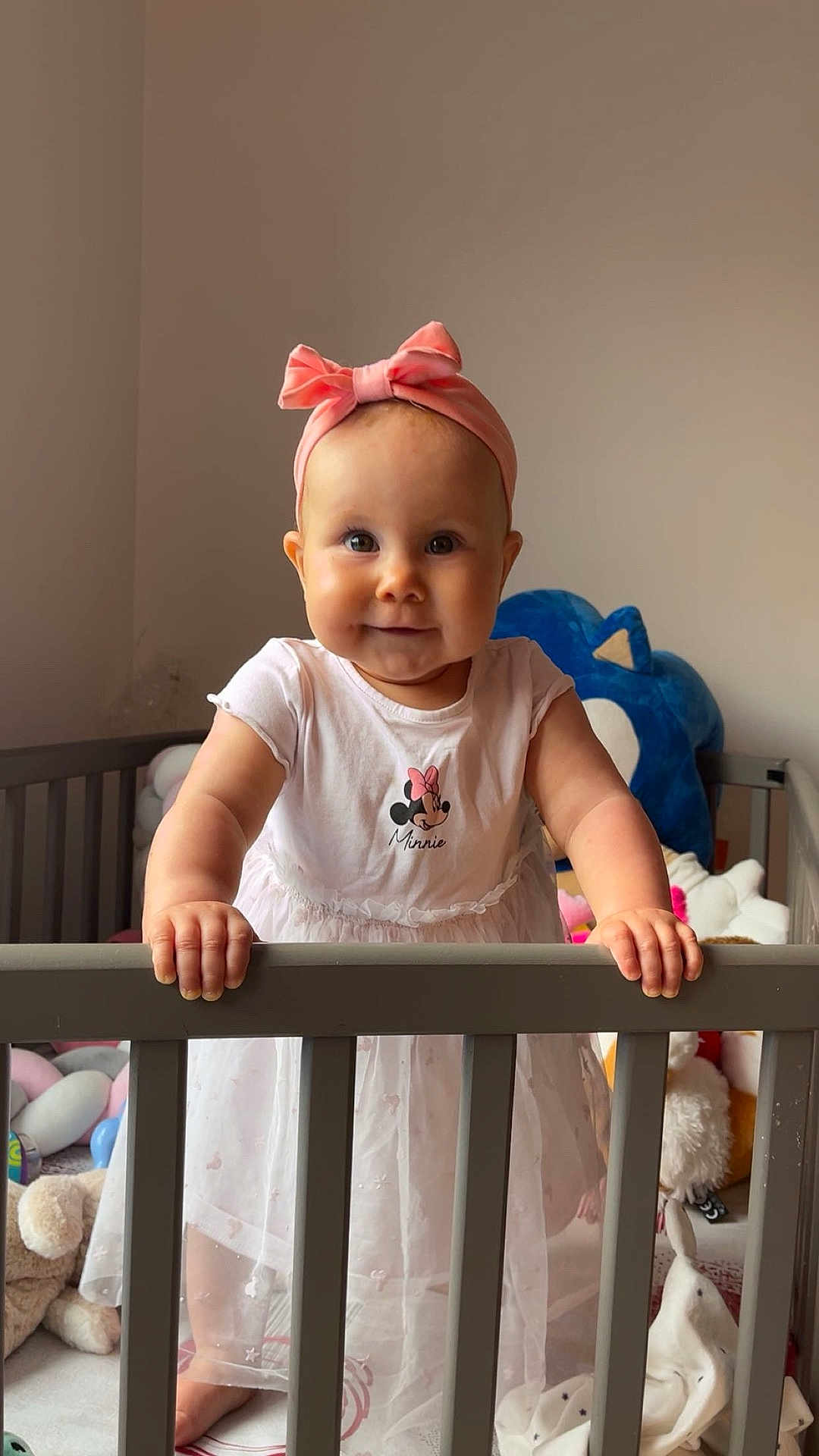 Julliana participe au concours pour gagner de l'argent avec cette photo : baby, child, crib, cute, dress, face, hand, happy, headband, indoor, infant, mickey_mouse, person, pink_bow, plush_toys, smile, standing, stuffed_animals, toy, white_dress