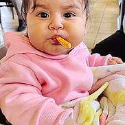 Lia joined the competition — help win amazing prizes! baby, child, face, french_fry, food, pink_hoodie, blanket, high_chair, hand, indoor, restaurant, tile_floor, person, cute, young_child, expression, snack, seated, hair, cozy